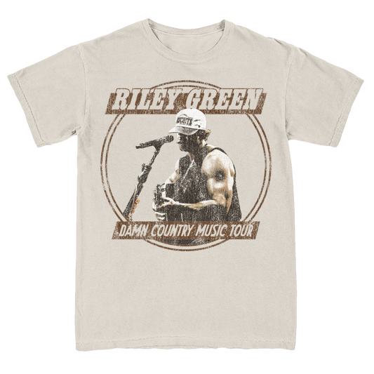 A tan-colored t-shirt with a graphic print of a person singing into a microphone and the text 'Damn Country Music Tour'. The shirt has a round neckline and short sleeves.