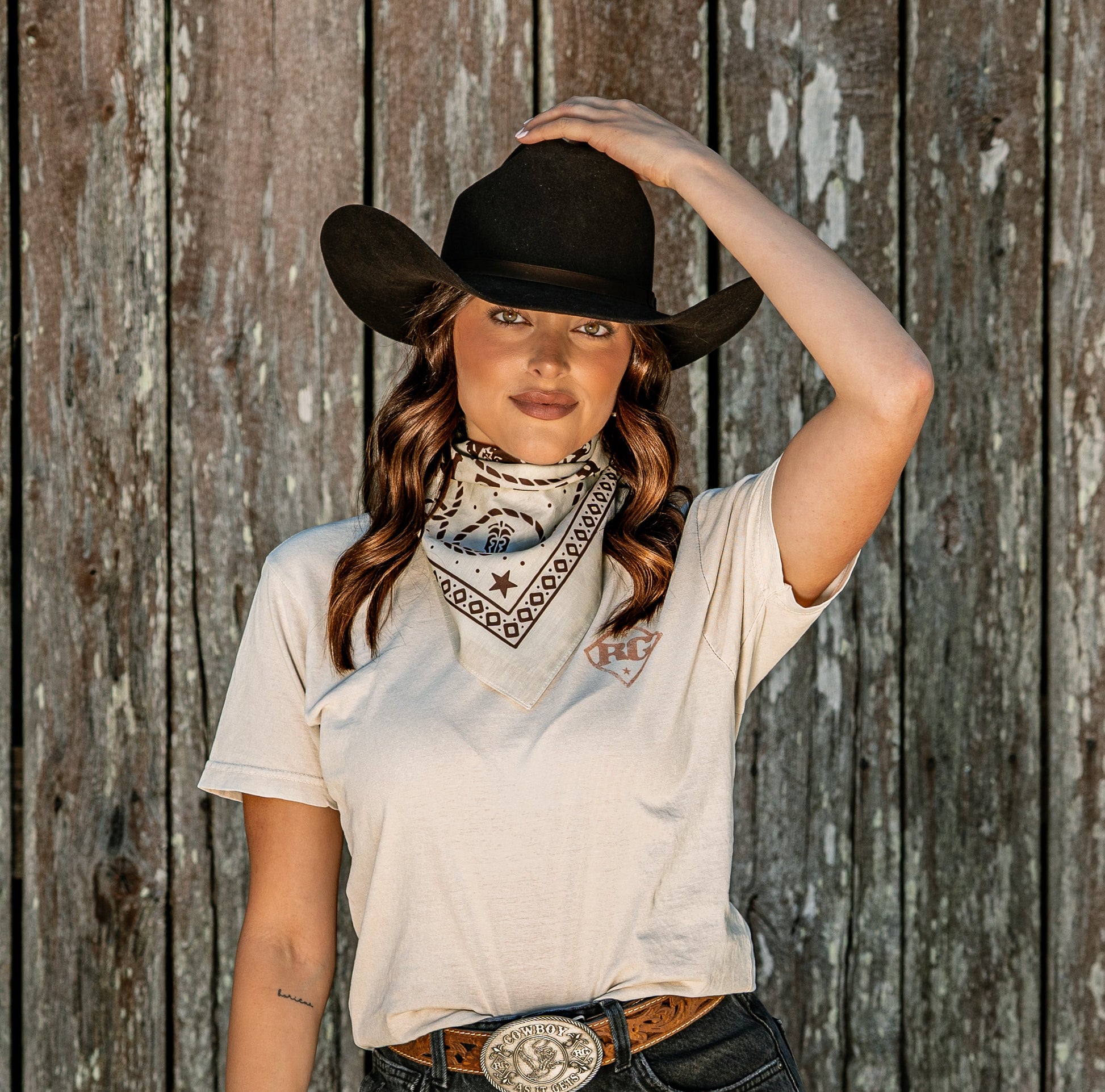 Person wearing a cowboy hat and bandana against a wooden fence background